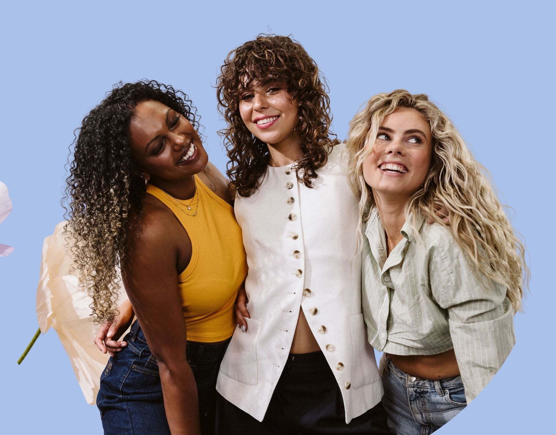 three women smiling with their arms around each other, with brunette, blonde and black coily, curly and wavy hair