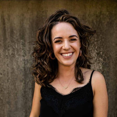 caucasian woman with voluminous brunette wavy hair against a stone background smiling