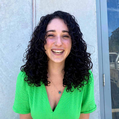 caucasian woman smiling with thick black 3b curly hair wearing a green shirt