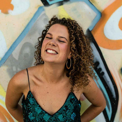 caucasian woman smiling with brunette and blonde 3b curly hair against a spray painted background